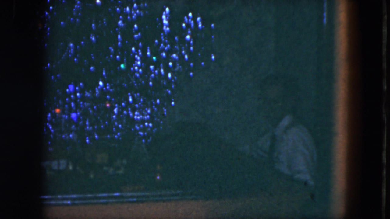 1951 Cleveland home-movie frame with a shadowed figure at a piano and scattered blue and red lights across the background.