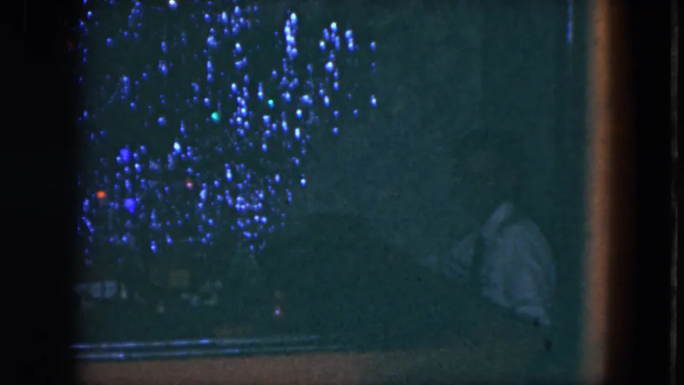 1951 Cleveland home-movie frame with a shadowed figure at a piano and scattered blue and red lights across the background.