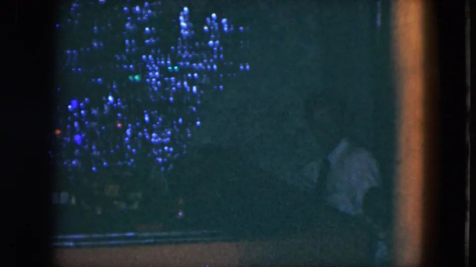 1951 Cleveland 8mm frame showing a faint seated figure near a piano, with dense grain and blue decorative lights in the dark.