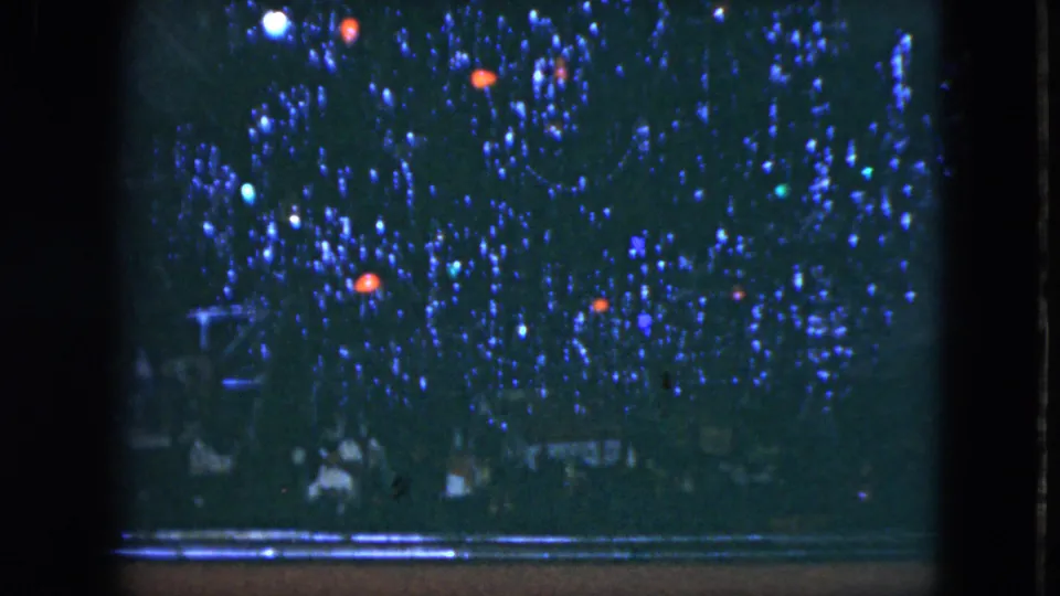 1951 Cleveland home-movie frame showing blue Christmas lights, red ornaments, and faint figures below in a dark night scene.