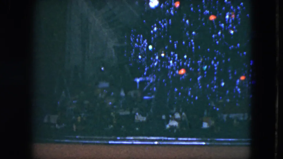 1951 home-movie view of blue Christmas lights and small red ornaments, partly obscured by dark framing and low exposure.