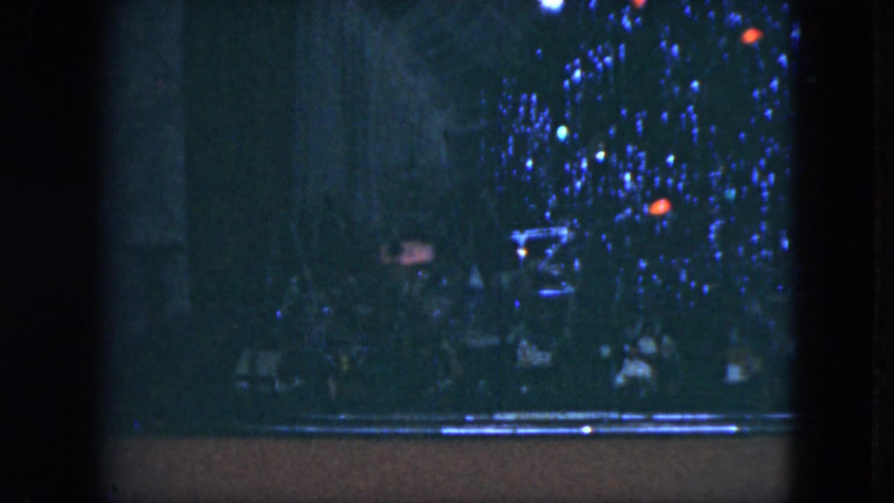 1951 Cleveland home-movie frame showing a dim Christmas tree display with colored lights and a horizontal ledge or track near the bottom.