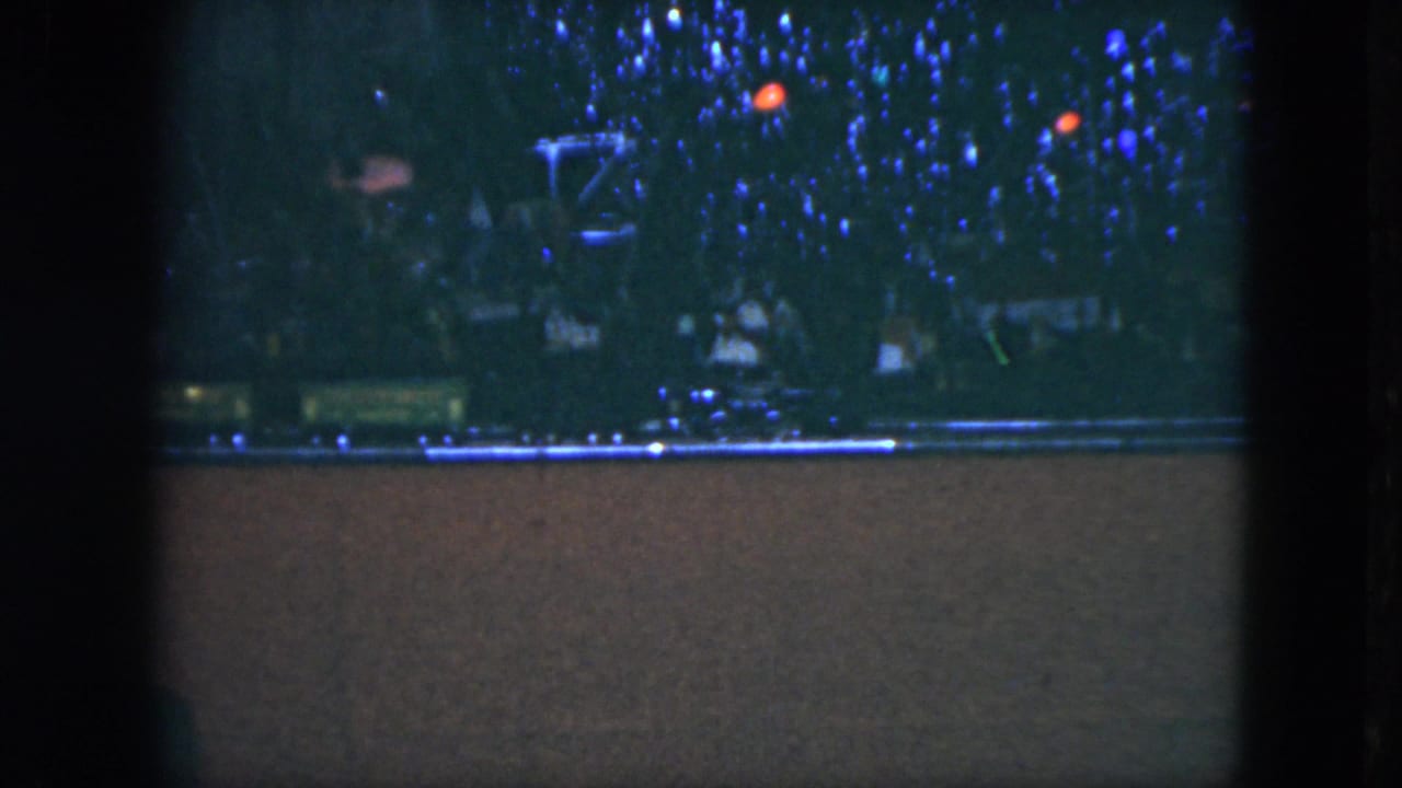 Model train on tracks beneath blue Christmas tree lights in a dark room.