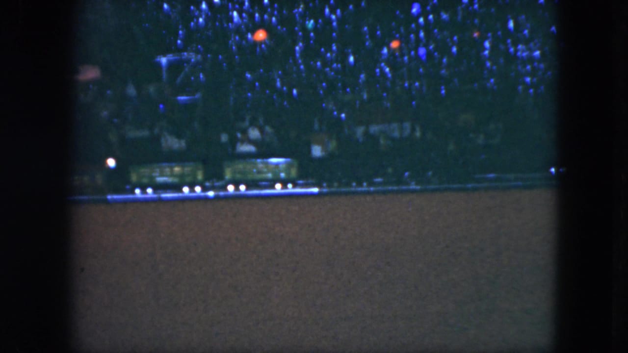 Model train cars move along a low track below Christmas lights.