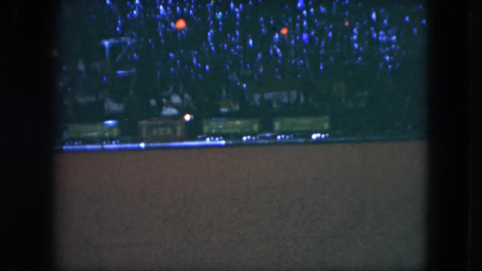 1951 Cleveland home-movie still showing a toy train display under blue-lit Christmas branches.