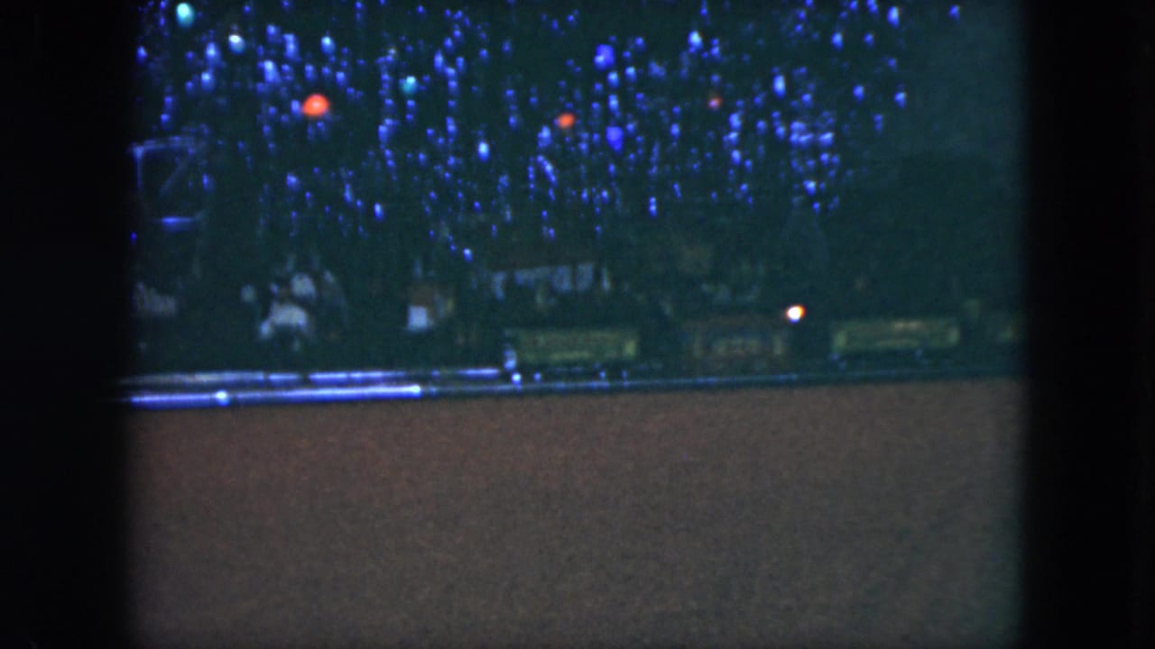 Toy train track in a dark room beneath dense blue and red decorative lights.