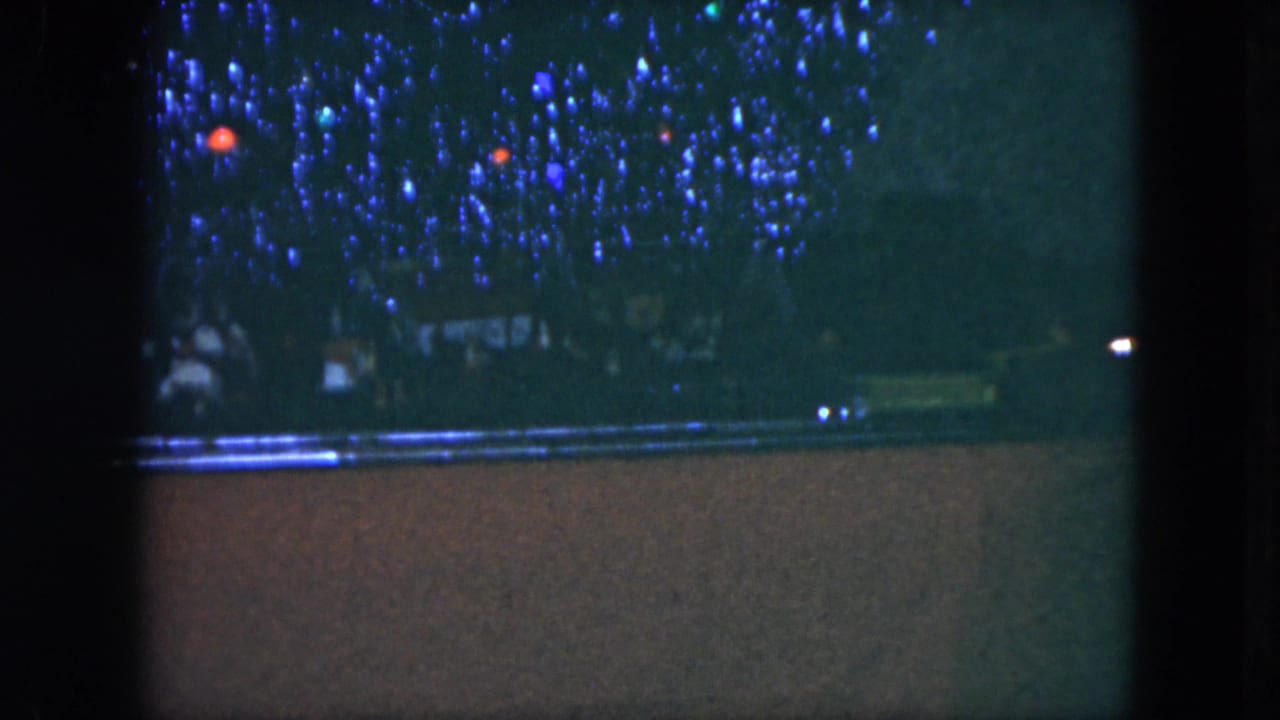 1951 Cleveland 8mm frame with a toy train layout in low light, blue decorative lights, and track visible across the lower frame.