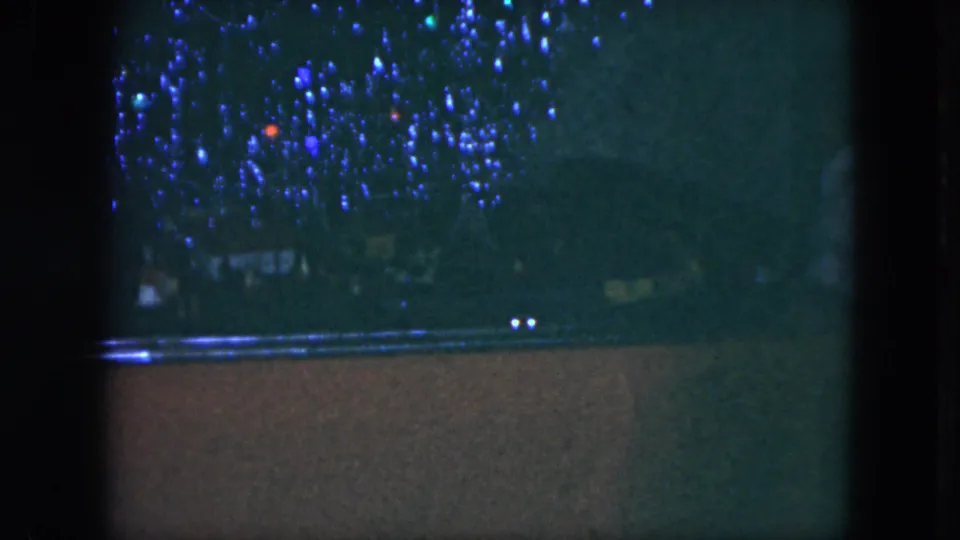 1951 Cleveland home-movie still showing a dim toy train setup with blue lights above the tracks and small bright points near the foreground.