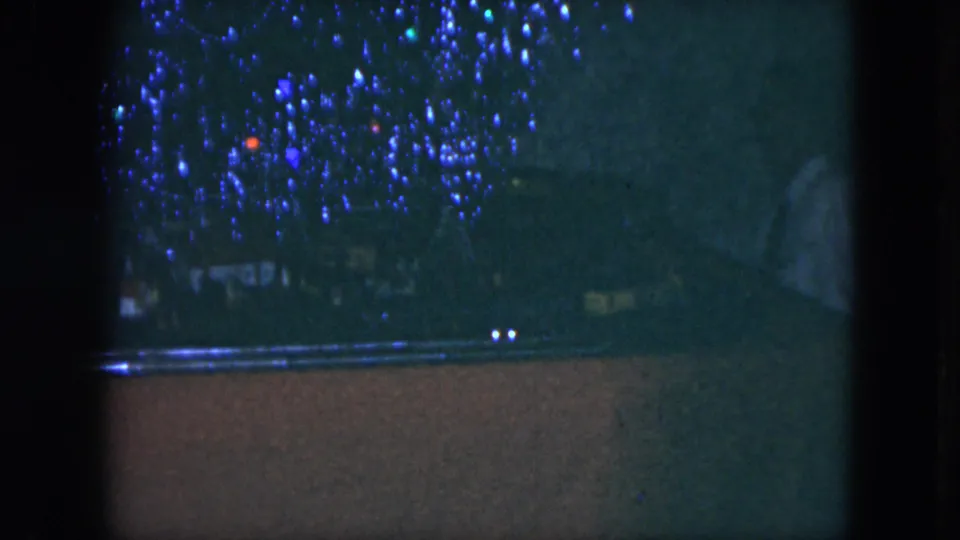 1951 Cleveland 8mm frame with toy train tracks, blue decorative lights, and a partially visible adult figure near the right edge.