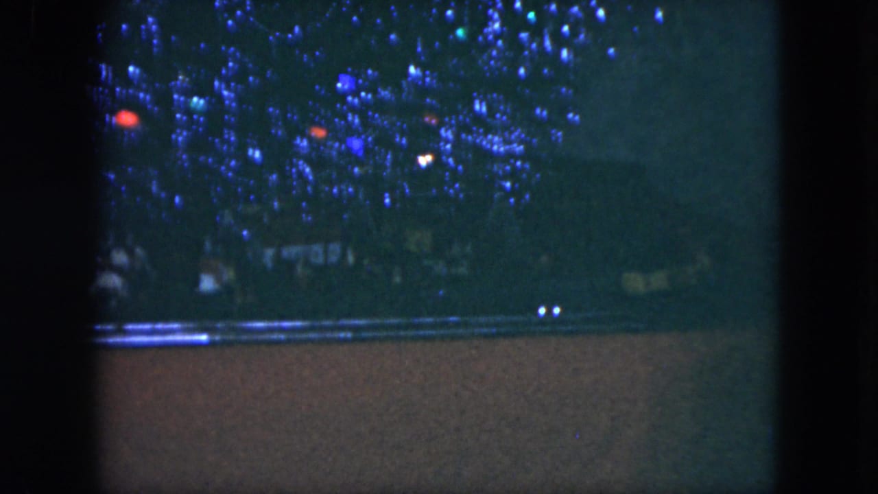 Dim nighttime crowd behind blue and red decorative lights with dark film borders.
