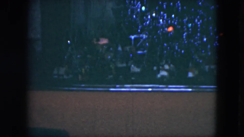 1951 Cleveland home-movie still with indistinct spectators, blue decorative lights, and a low foreground band in darkness.