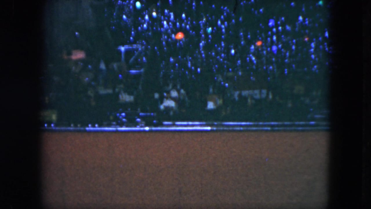 Decorated tree and model train track visible in a dark, grainy holiday interior frame.