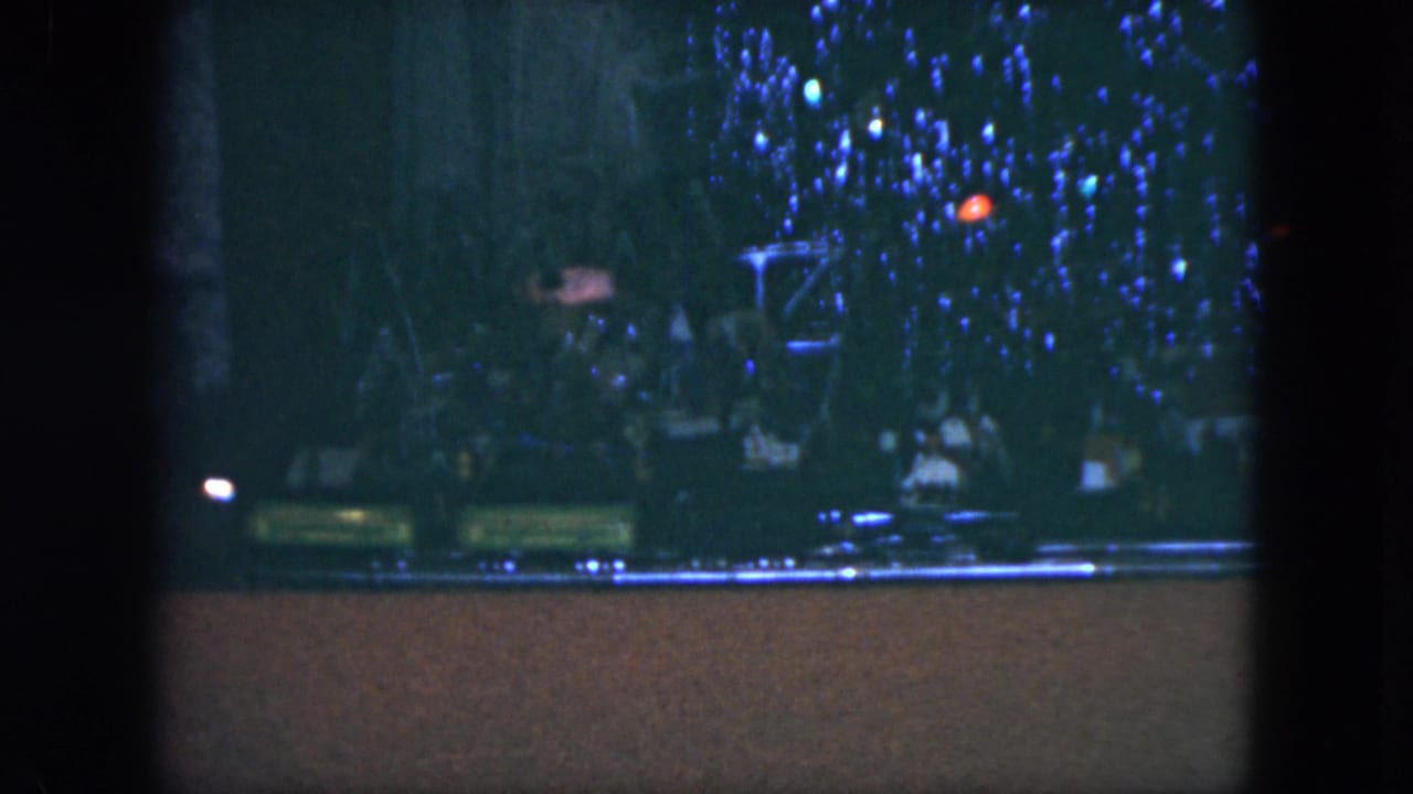 Green toy train car passes below a lit Christmas tree display.