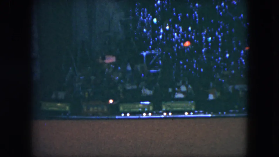 1951 Cleveland 8mm view of several toy train cars beneath a Christmas tree display glowing with blue and red lights.