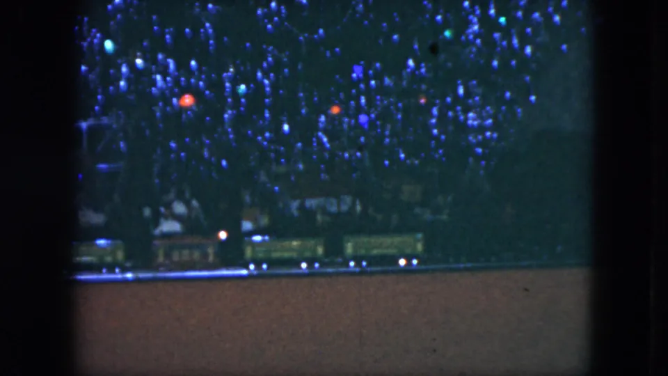 Final 1951 Cleveland frame with a toy train at the bottom of a dense blue-lit Christmas tree display, seen through dark window divisions.