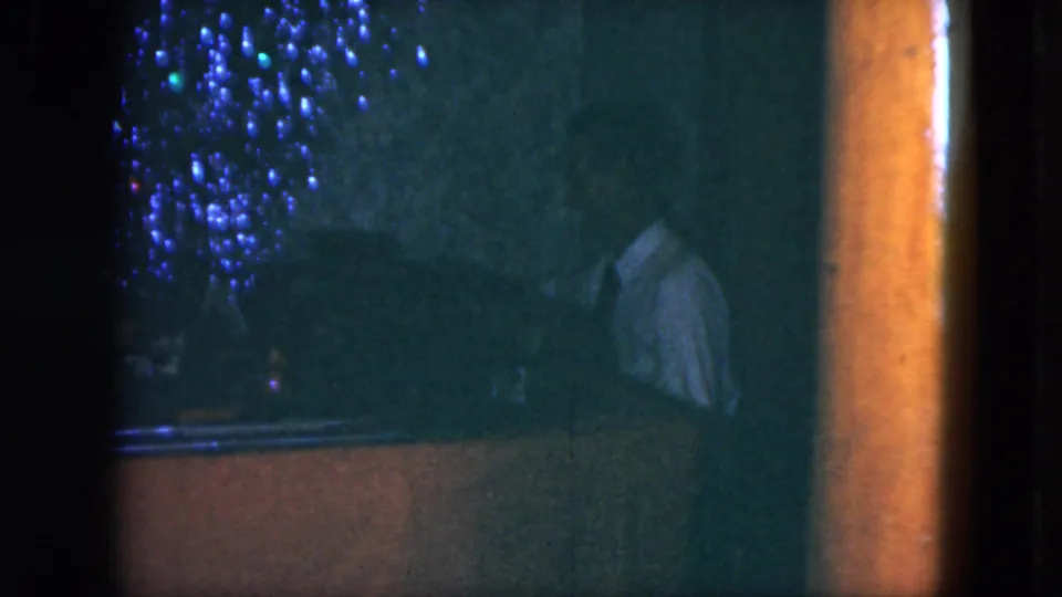 Dim 1951 Cleveland home-movie frame of the train display, with blue lights, glassy reflections, and dark interior framing.
