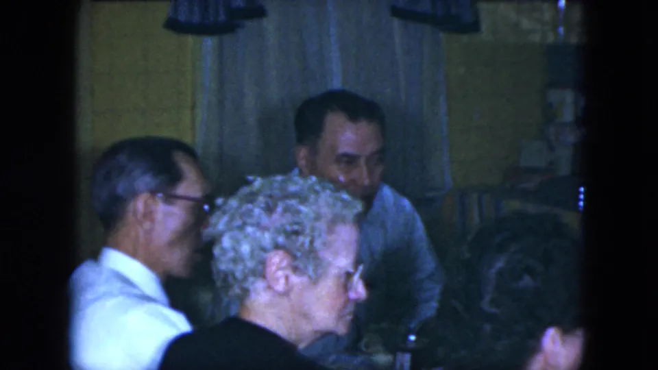 1951 Cleveland home-movie frame showing older adults gathered in a warm interior near the miniature train display.
