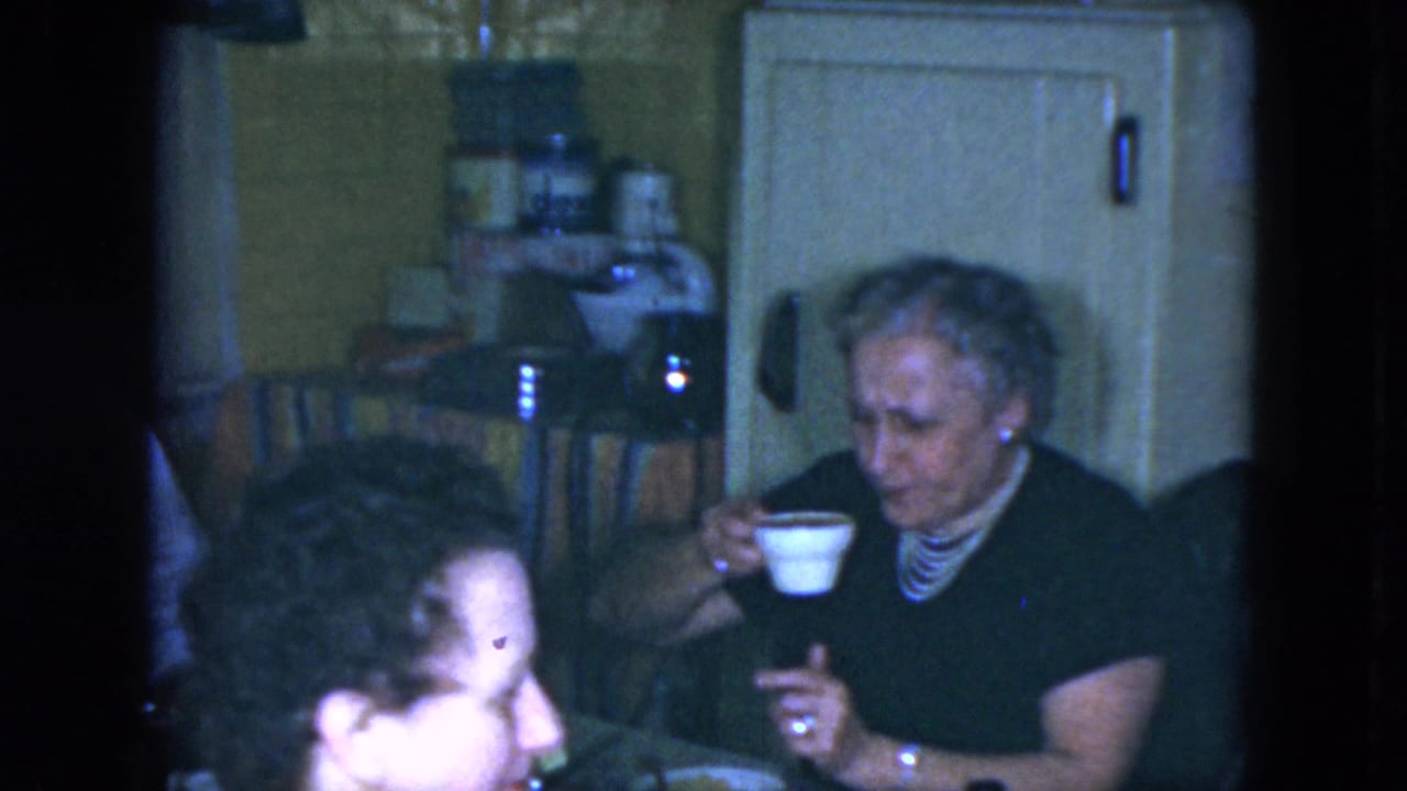 Older woman drinks from a cup while seated at a table.