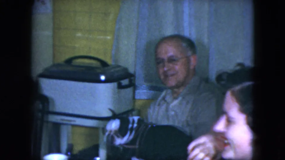 1951 Cleveland home interior with a smiling seated man, a small black-and-white dog, and another person partly visible in the foreground.