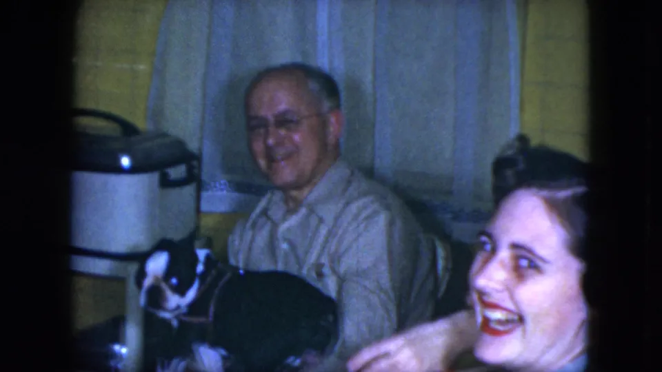 A laughing woman enters the side of the 1951 Cleveland kitchen scene while an older man sits with a black-and-white dog.