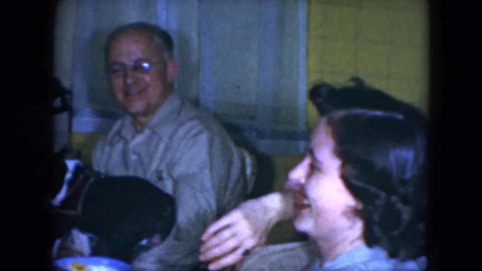 In the Cleveland home interior, a woman laughs in profile beside the seated older man and the small black-and-white dog.