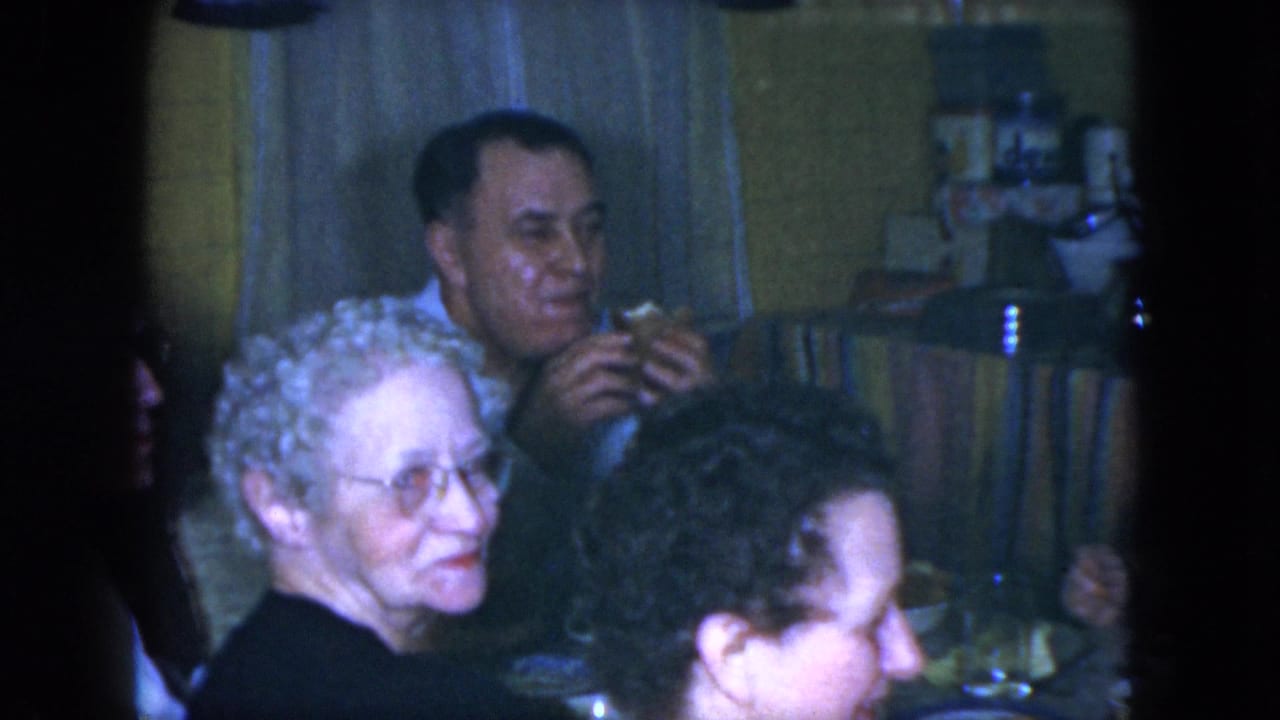 1951 Cleveland home interior with adults gathered at a dining table, including a curly-haired woman in the foreground and a man holding food.