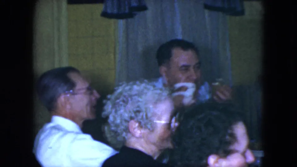 1951 Cleveland dining-room scene with adults seated around the table, one man in a light shirt seen in profile and others eating nearby.