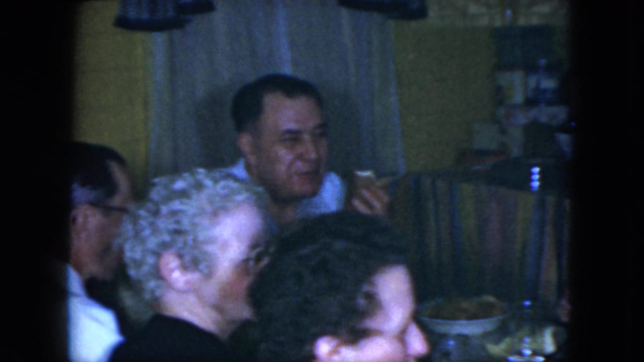 Older adults sit close together at a dining table in a home kitchen.
