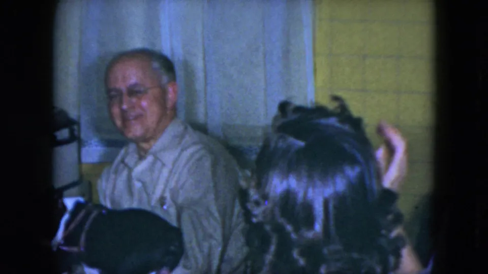 An older man wearing glasses smiles from a seat at the dining table in the Cleveland home interior.