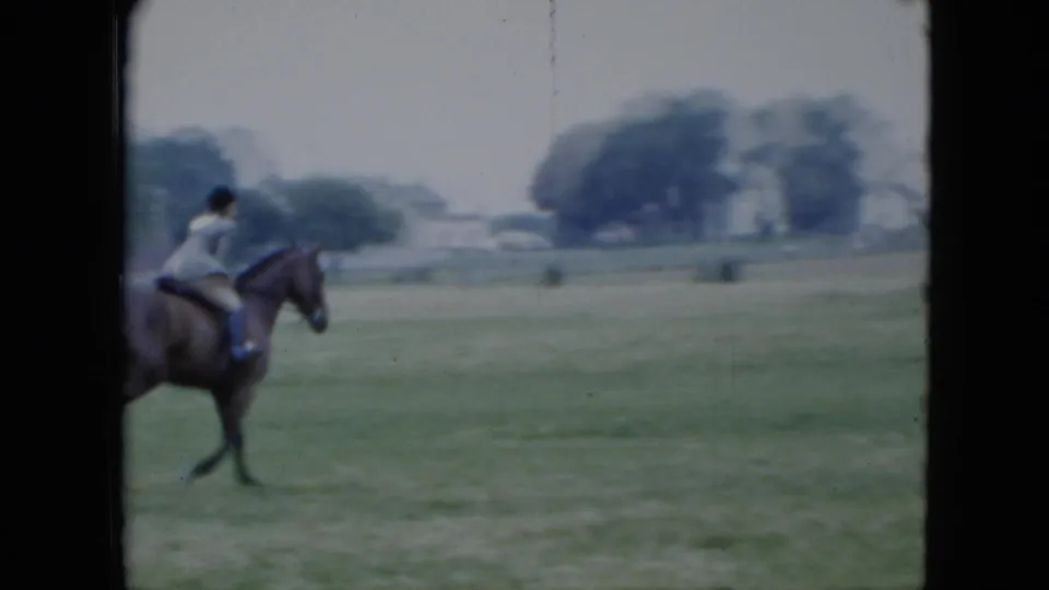 In 1951 Cleveland home-movie footage, a woman rides a dark horse across an open grassy field with distant houses and trees.