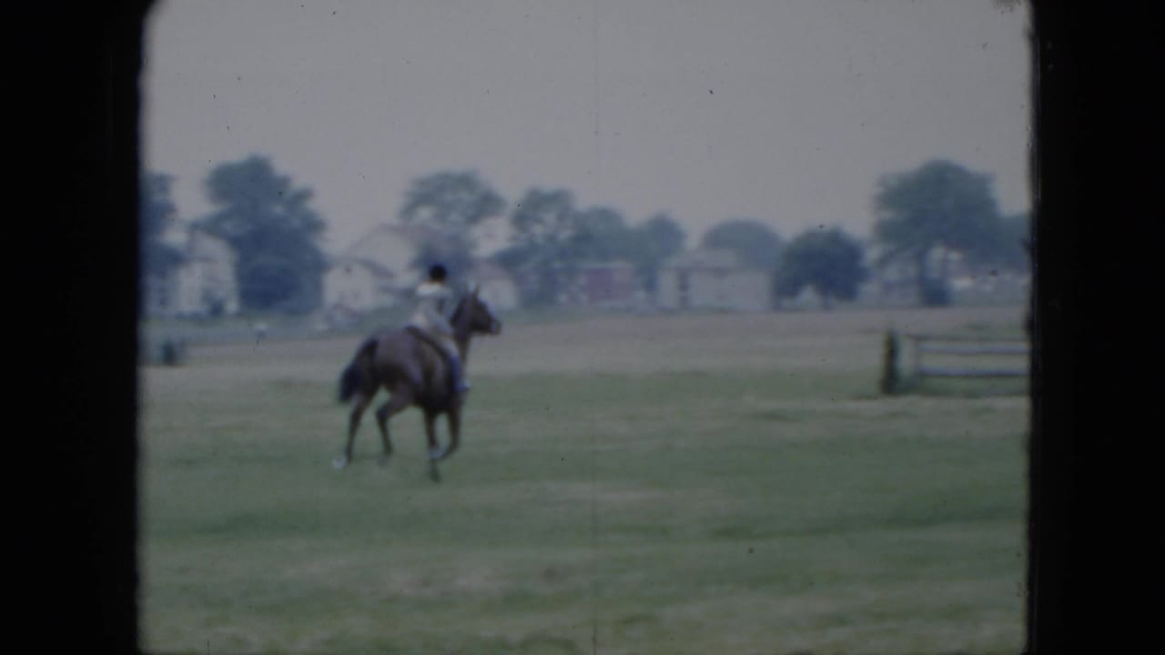The rider continues across the Cleveland field on horseback, moving toward distant houses, trees, and a low fence line.