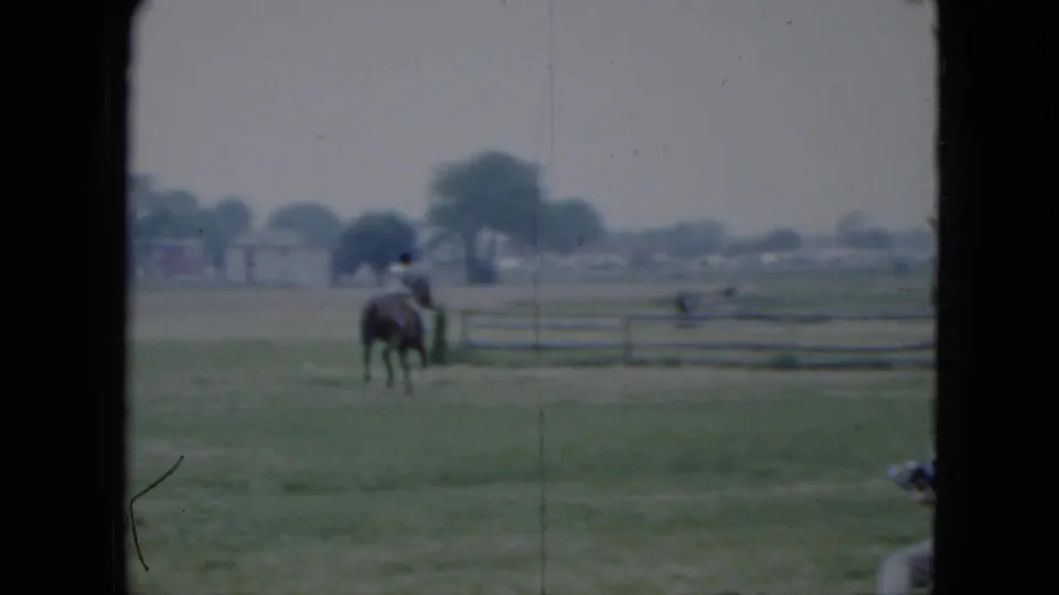 The woman on horseback appears near a wooden rail fence in the 1951 Cleveland field, with houses and trees in the background.