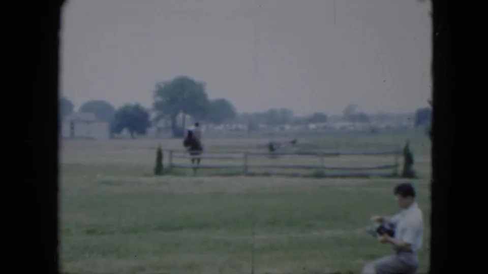 The rider is near the fence as a man holding a camera appears at the lower right of the 1951 Cleveland home-movie frame.