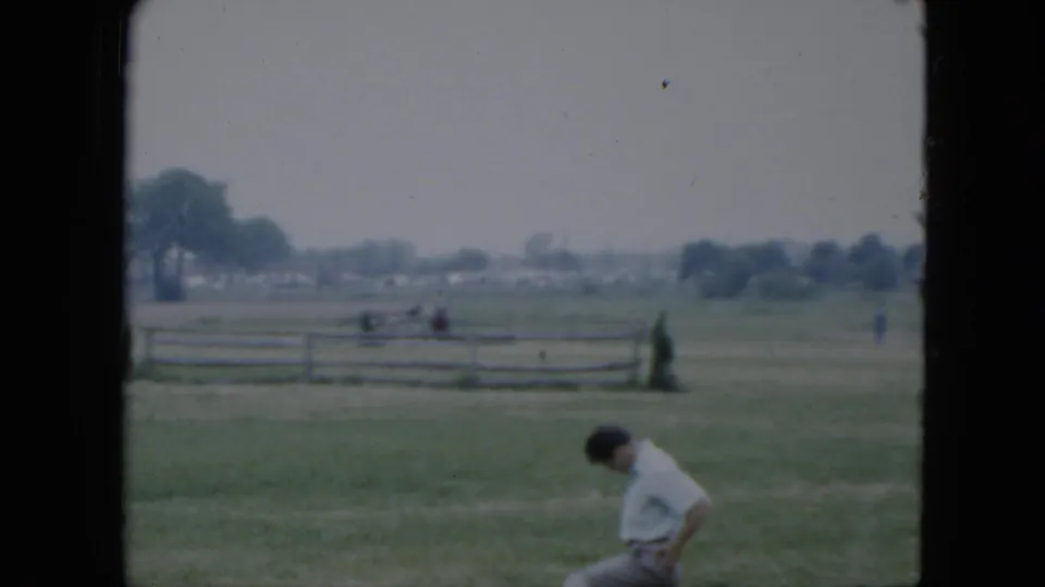 1951 Cleveland-area frame with the seated man partly low in view and a rider continuing across the fenced grassy field.