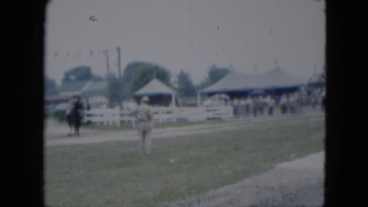 1951 Cleveland fairground view with a horseback rider, white rail fencing, tents, and spectators in the background.