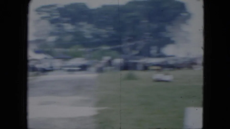 Motion-blurred 1951 Cleveland home-movie frame showing parked cars, trees, people, and open grass near the fairground.