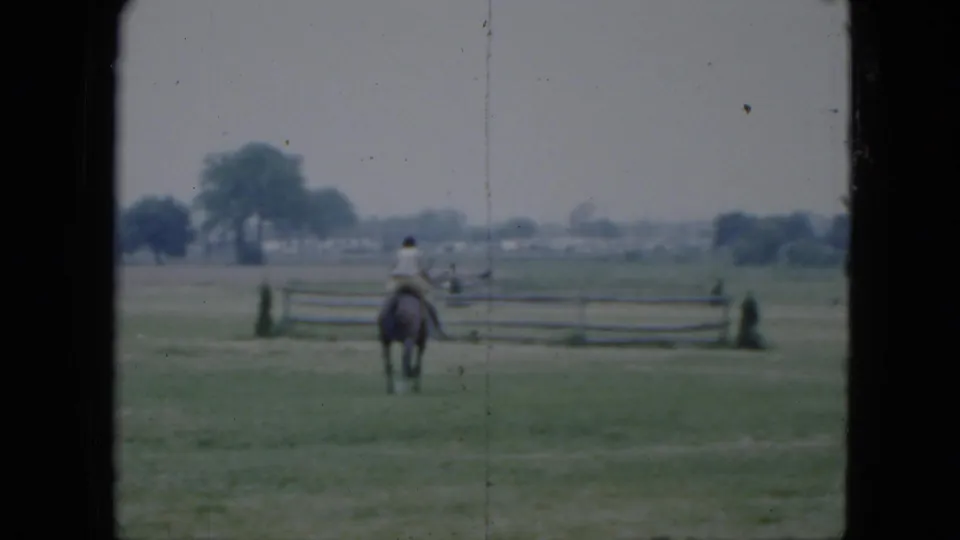 The rider and dark horse are seen from behind in the Cleveland field, heading toward a wooden rail fence under a pale sky.