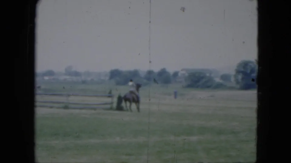 The horse and rider remain near the fence in the 1951 Cleveland field, with distant trees, low structures, and visible 8mm wear.