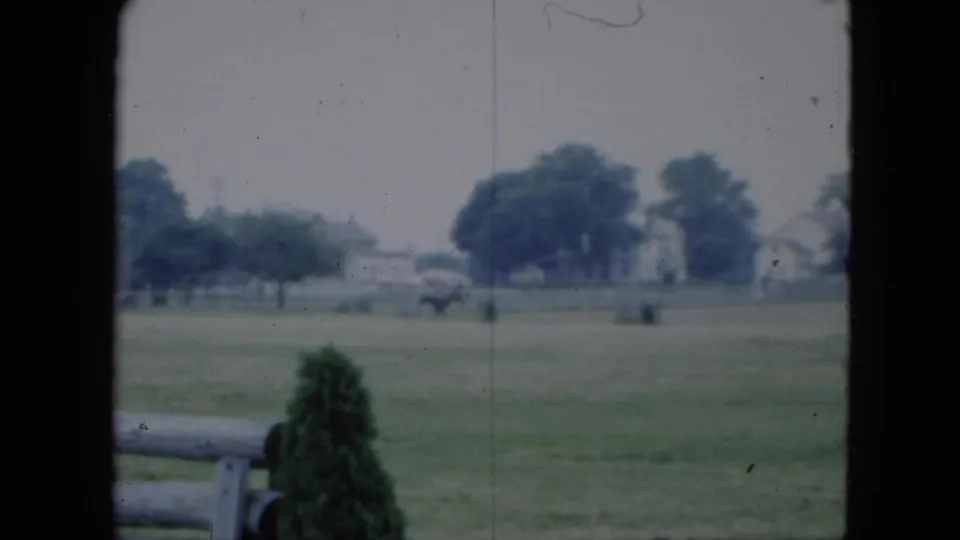 1951 Cleveland home-movie still showing the rider and horse near the middle distance, with fence rails and houses visible.