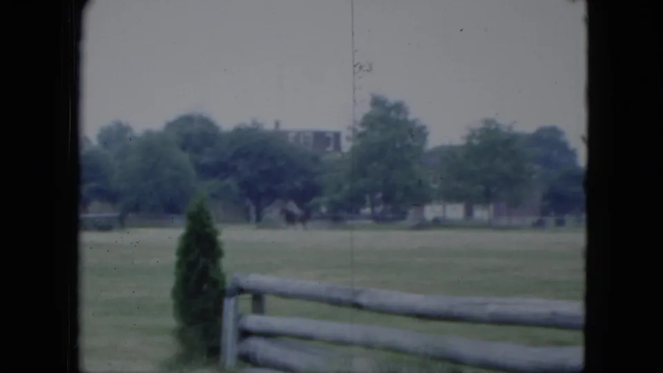 1951 Cleveland 8mm frame with a distant horse and rider moving across a green field behind a split-rail fence.