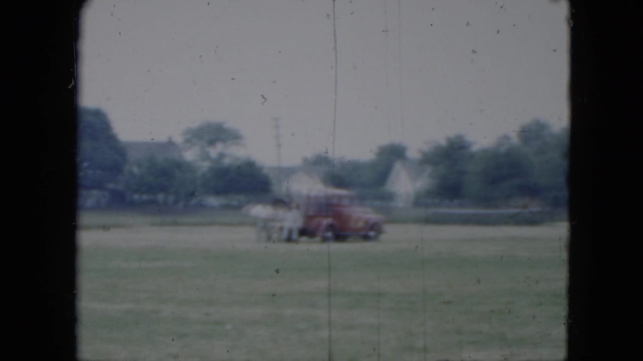 1951 Cleveland-area home-movie frame with a horse and rider moving near a red truck across a broad grass field.