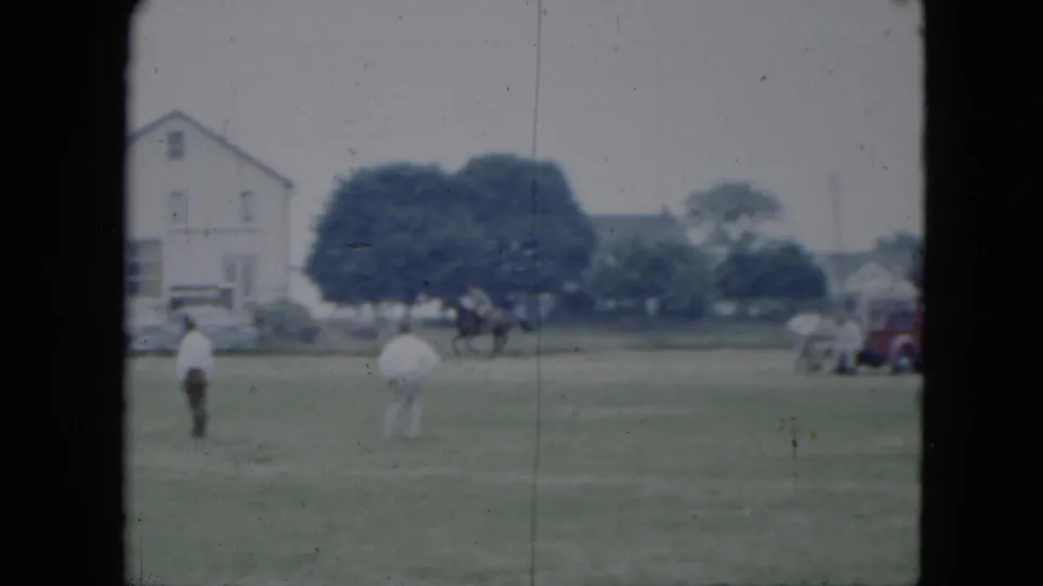 1951 Cleveland-area 8mm frame showing two people crossing a field, with a horse and rider, red truck, house, and trees behind them.