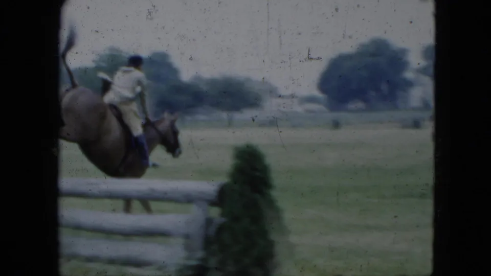 Horse and rider move through the frame near a white rail fence at the 1951 Cleveland equestrian grounds.