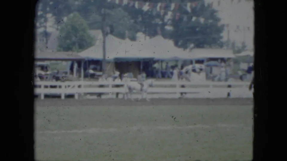 Tents, white fences, and distant visitors line the edge of a Cleveland equestrian field in soft 8mm footage.