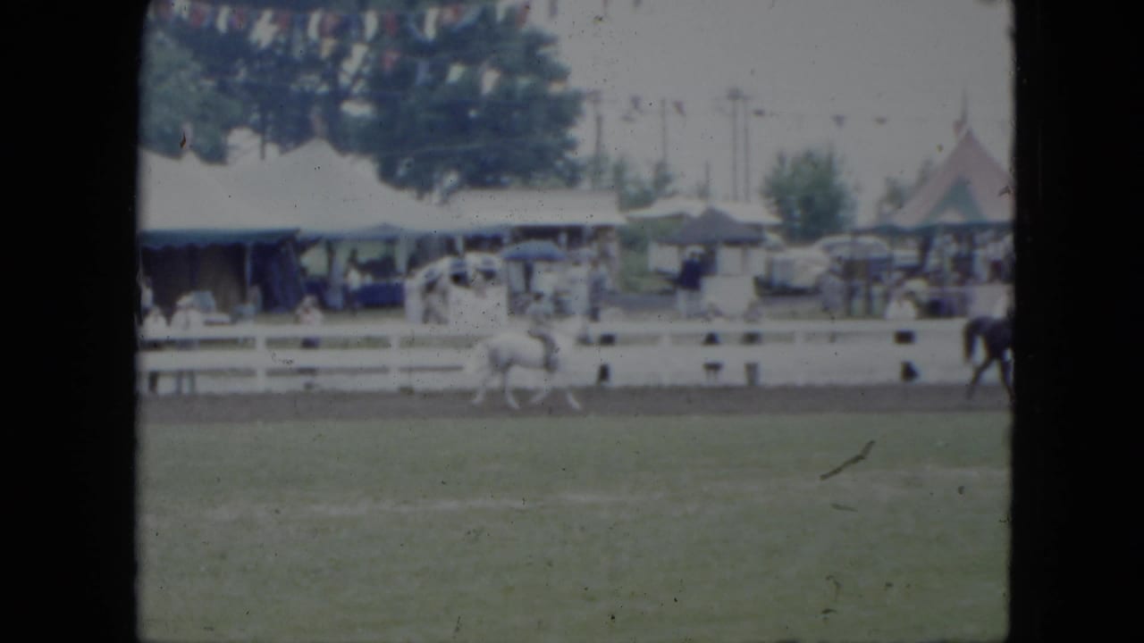 1951 Cleveland footage frame with a white horse and rider trotting along a dirt track in front of spectators and fair tents.