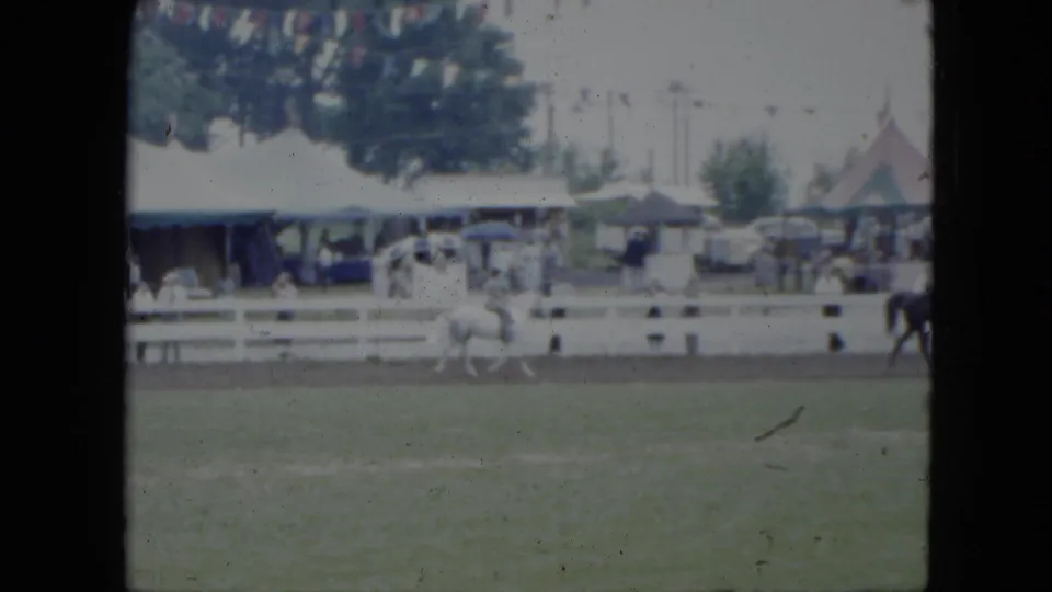 1951 Cleveland footage frame with a white horse and rider trotting along a dirt track in front of spectators and fair tents.