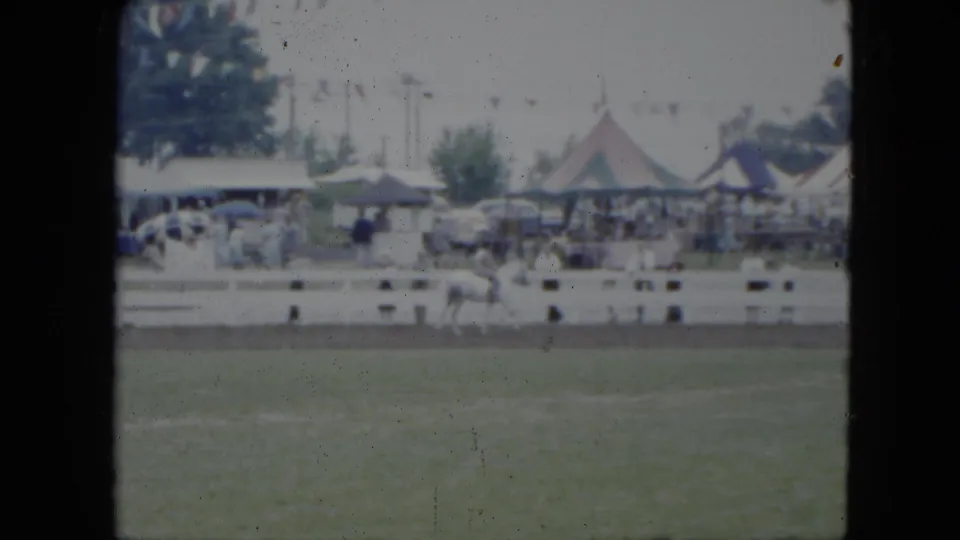 1951 Cleveland frame showing a white horse and rider near the fence line, with spectators, tents, and parked cars beyond.