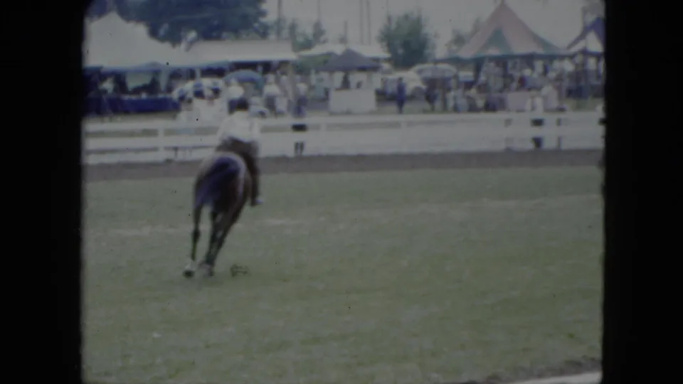 The rider and brown horse move away from the camera across the Cleveland equestrian ring, framed by spectators and tents.