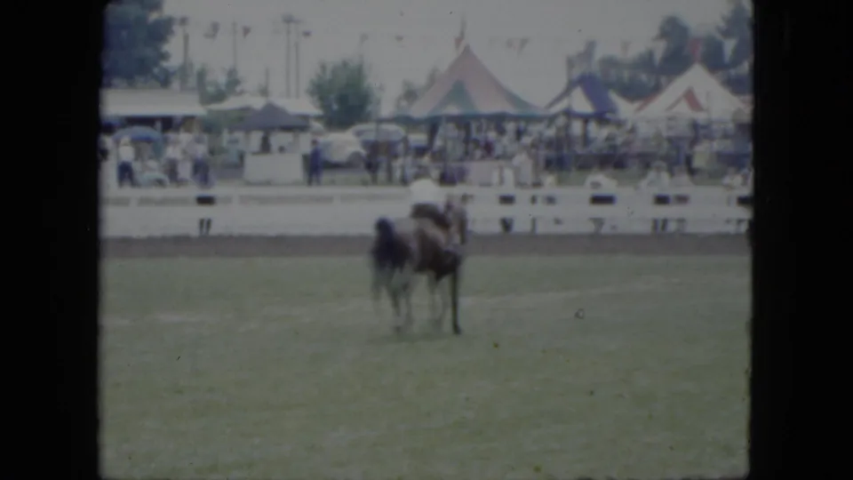 A distant view shows the horse and rider continuing through the 1951 Cleveland ring while spectators watch from behind fencing.