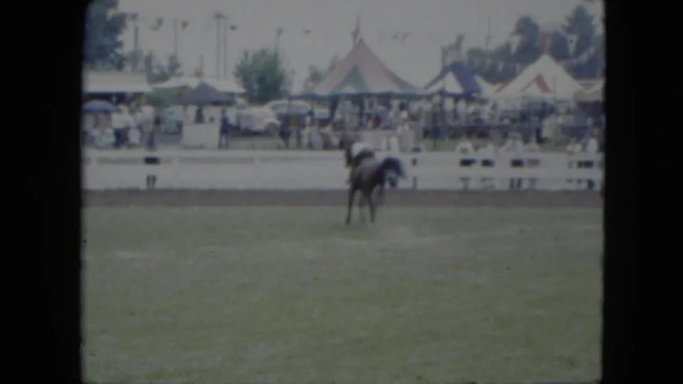 1951 Cleveland fairground view with a horse and rider moving across a grassy field before distant spectators, tents, trees, and automobiles.